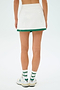 Someone wearing the SPLITS59 Monah Rigor Skort in White/Arugula, paired with white socks featuring green stripes and white sneakers with blue logos, stands against a plain background.