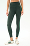 A person wears SPLITS59 Amber Airweight High Waist 7/8 leggings in Military/Spearmint, featuring a comfy nylon-spandex blend and green side stripe, paired with white sneakers with green stripes, standing against a white background.