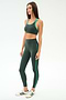 A woman stands in profile against a white background, wearing SPLITS59's Amber Airweight High Waist 7/8 leggings and sports bra in Military/Spearmint, crafted from a comfortable nylon-spandex blend.