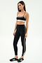Woman stands in studio wearing the SPLITS59 Scottie Airweight Bra in Black/Lentil and matching high-waisted leggings with beige side stripes, paired with black Adidas sneakers.