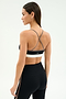 A woman faces away, wearing the SPLITS59 Scottie Airweight Bra in Black/Lentil and black high-waisted leggings against a plain light background.