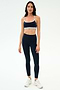 A woman stands facing forward in SPLITS59's Emerson Airweight High Waist leggings in Indigo/Dove Grey with a matching sports bra and white sneakers—perfect for Pilates or hot yoga—against a plain light background.
