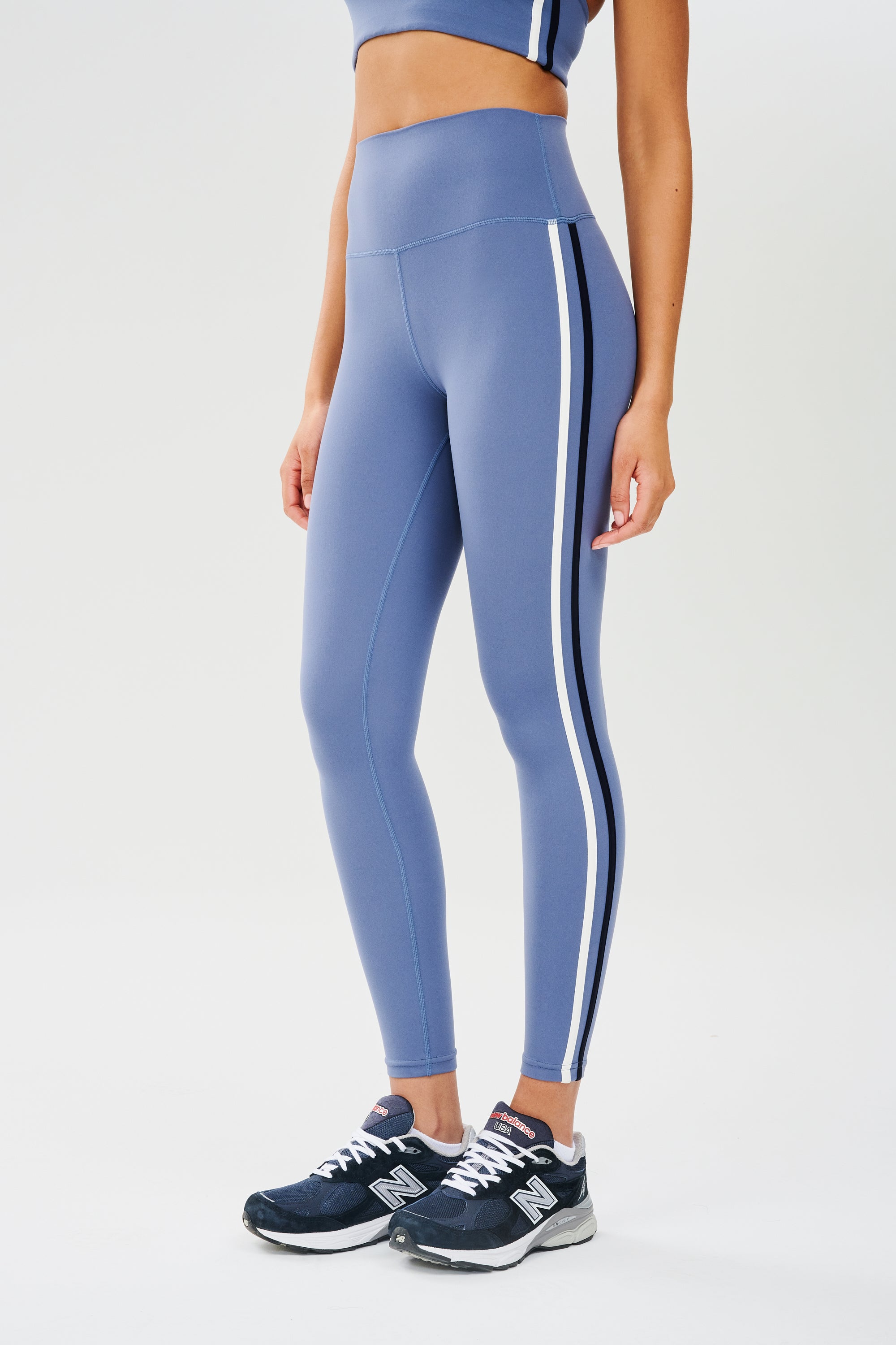 Side view of girl wearing light blue leggings with thin white and black stripes down the side with dark blue shoes