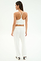 A woman faces away, wearing SPLITS59's Andie Oversized Fleece Varsity 59 Sweatpant in White/59 with a white sports bra and black-striped slide sandals, perfect for cool weather workouts, set against a plain white background.