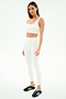 A woman stands against a white background wearing the SPLITS59 Airweight Rib Bra in white, paired with matching high-waisted leggings made from moisture-wicking ribbed fabric and black Adidas sneakers—ideal for hot yoga.