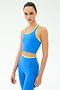 A woman wears the SPLITS59 Amber Airweight Bralette in Classic Blue/Ray, featuring a scoop neck and yellow trim, paired with matching high-waisted leggings, standing against a plain light background.