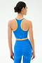 A woman faces away, wearing the SPLITS59 Amber Airweight Bralette in Classic Blue/Ray and matching high-waisted leggings with yellow trim, set against a plain light background.