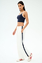 A woman poses in a navy crop top, SPLITS59 Maxie Rigor Track Pant - White/Indigo, and white sneakers with red stripes.