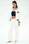 A woman in the SPLITS59 Hayes Varsity Rigor Jacket in white, paired with white track pants, a navy crop top, and white sneakers with red stripes, stands against a plain white background.