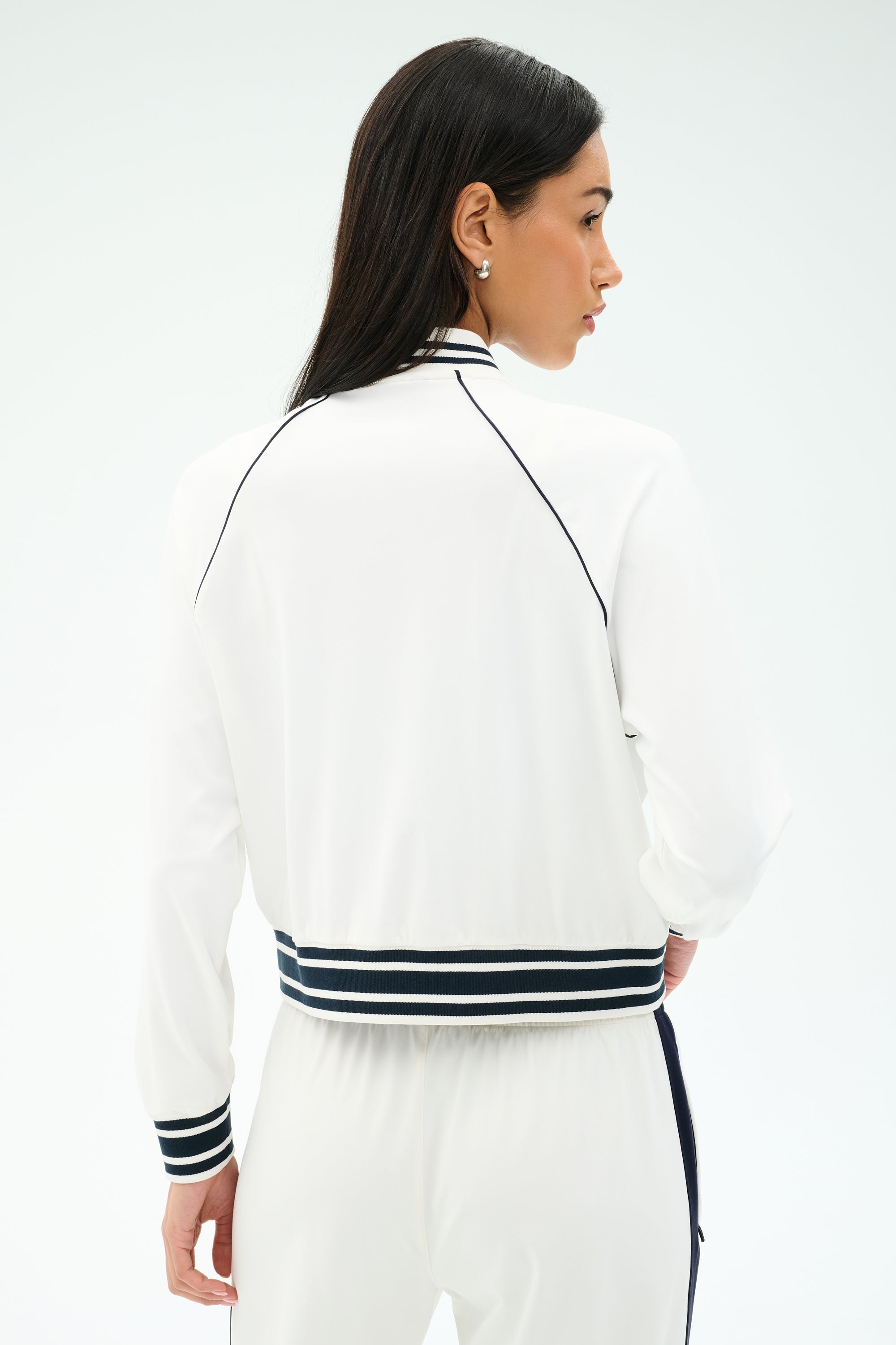 A woman is shown from the back wearing the SPLITS59 Hayes Varsity Rigor Jacket in white, featuring black trim and striped cuffs, paired with matching pants.
