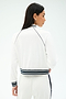 A woman is shown from the back wearing the SPLITS59 Hayes Varsity Rigor Jacket in white, featuring black trim and striped cuffs, paired with matching pants.