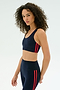A woman with curly hair wears the SPLITS59 Ella Airweight Bra in Indigo/Pirate Red, standing against a plain white background.