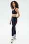 A person wears the SPLITS59 Ella Airweight Bra in Indigo/Pirate Red, paired with matching leggings, white socks, and silver sneakers, standing against a plain light background.