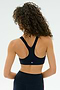 A person with curly hair is shown from the back wearing the SPLITS59 Ella Airweight Bra in Indigo/Pirate Red, paired with high-waisted spandex leggings, against a plain light background.