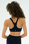A person with curly hair is shown from the back wearing the SPLITS59 Ella Airweight Bra in Indigo/Pirate Red, paired with high-waisted spandex leggings, against a plain light background.