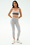 A woman stands against a white background wearing the SPLITS59 Emerson Airweight High Waist leggings in Dove Grey/Indigo and a light gray sports bra, perfect for hot yoga or Pilates, paired with white athletic shoes.