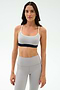 Woman wearing the SPLITS59 Emerson Airweight Bra in Dove Grey/Indigo with thin straps and high-waisted leggings, ideal for hot yoga or Pilates, stands against a plain white background.