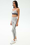 A woman wears the SPLITS59 Emerson Airweight Bra in Dove Grey/Indigo and matching high-waisted leggings, ideal for Pilates or hot yoga. She pairs them with white sneakers and stands against a plain white background.