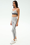 A woman wears the SPLITS59 Emerson Airweight Bra in Dove Grey/Indigo and matching high-waisted leggings, ideal for Pilates or hot yoga. She pairs them with white sneakers and stands against a plain white background.