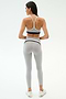 Wearing the SPLITS59 Emerson Airweight Bra in Dove Grey/Indigo, gray leggings with a black stripe, and white sneakers, a person stands facing away in a plain studio—ready for Pilates or hot yoga.