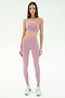 A woman poses in a studio wearing SPLITS59 Margot Rigor Leggings in Blush/Military and a matching light purple sports bra, paired with white athletic shoes.