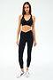 A woman faces forward against a plain white background, wearing SPLITS59’s Mia Rigor Legging w/ Stripe in Black/White, a black spandex sports bra, and white sneakers.
