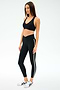 A woman wears the SPLITS59 Mia Rigor Bra in black with matching leggings featuring a white side stripe and white sneakers, standing against a plain light background—ideal for gym workouts or multisport performance.