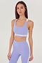 A woman wearing a stylish SPLITS59 Miles Rigor Bra in Purple Haze paired with white workout leggings.