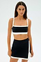 A woman in a SPLITS59 Monah Rigor Bra in black/white and skirt stands against a plain white background, showcasing firm support for intense gym workouts.
