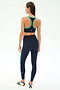 A woman, seen from behind, wears SPLITS59’s Amber Airweight High Waist 7/8 leggings in Indigo/Spearmint and a matching sports bra, paired with white sneakers featuring navy stripes, all set against a plain white background.