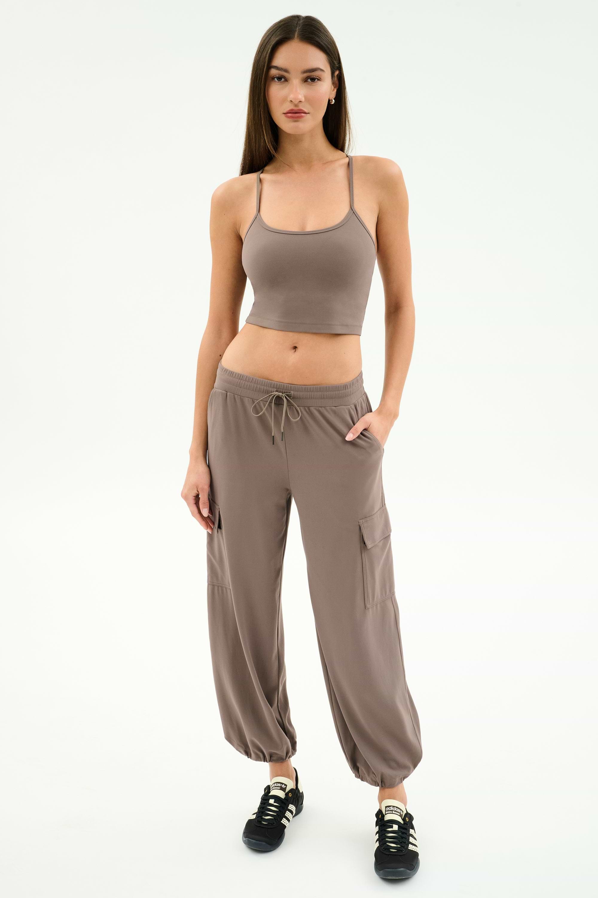 A woman faces forward wearing the SPLITS59 Airweight Crop in Lentil with matching taupe cargo pants and black sneakers against a white background—ideal for hot yoga or casual outings.