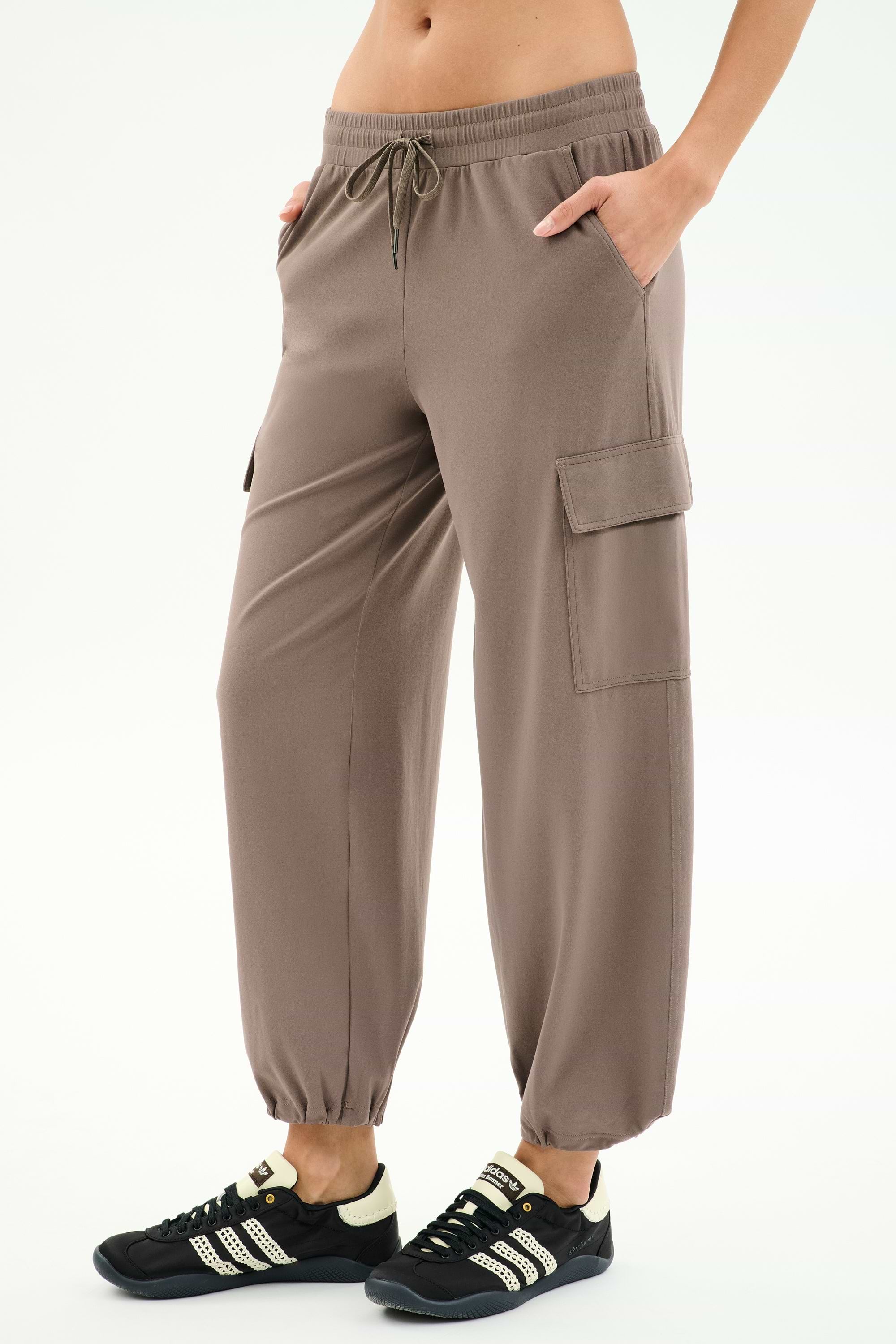 A person wears SPLITS59’s Nico Airweight Cargo Pant in Lentil, featuring a drawstring waist and side pockets, paired with black athletic shoes against a white background—ideal for workouts or casual outings.
