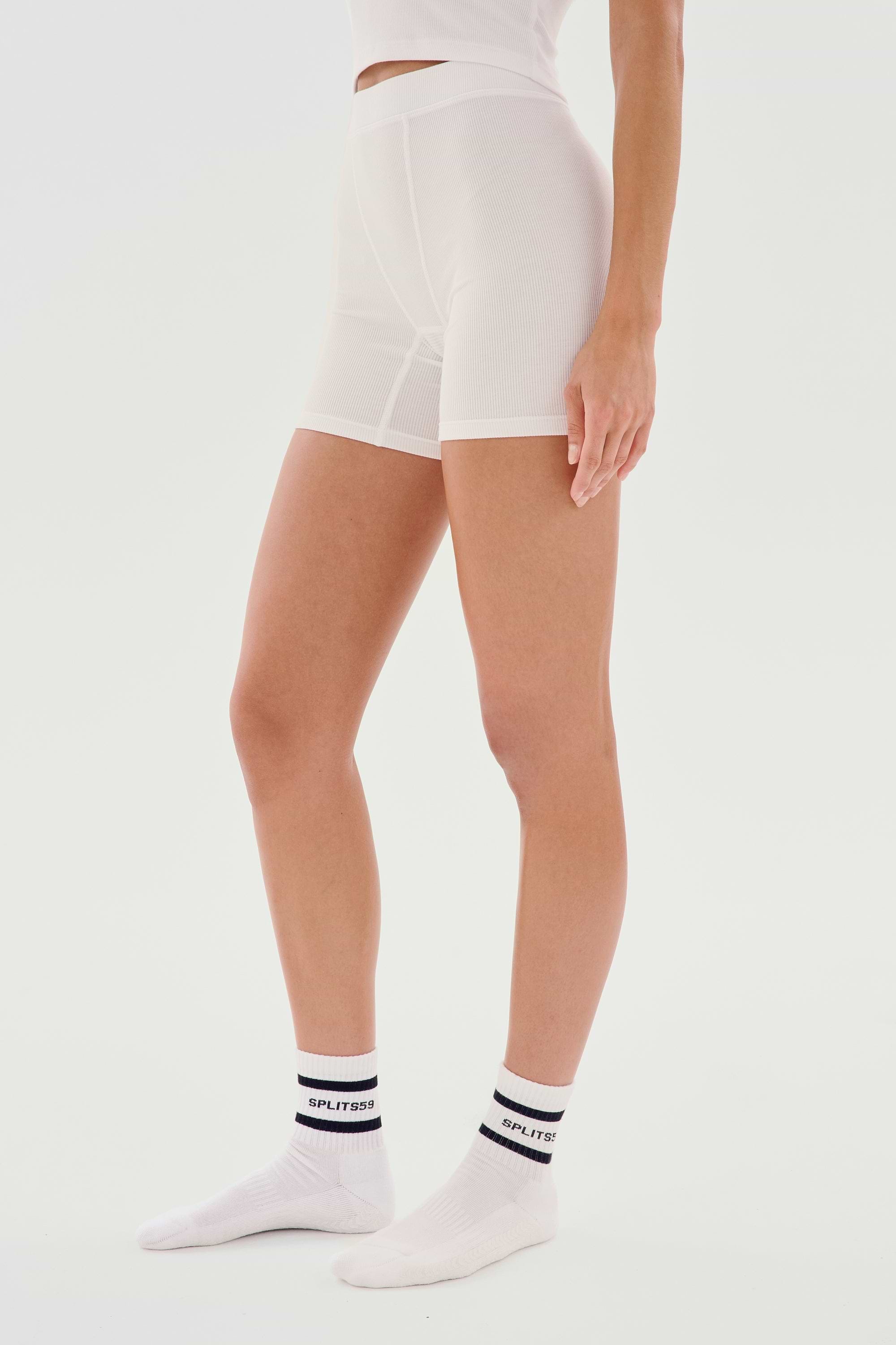 Person standing in white seamless fitted SPLITS59 Theo Rib Short - White and white socks with black and white logo. Cropped at chest level, side view against a plain white background, showcasing the tailored comfort of the SPLITS59 Theo Rib Short - White's classic design.