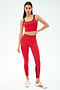 A woman poses against a plain backdrop in the SPLITS59 Cait Rigor Bralette in Pirate Red/Indigo, paired with matching high-waisted leggings detailed with black trim and white sneakers featuring red stripes.