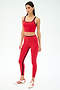 A woman wears the SPLITS59 Cait Rigor Bralette in Pirate Red/Indigo, paired with matching leggings and white athletic shoes with red stripes, standing against a plain white background.