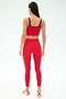 A woman faces away, wearing the SPLITS59 Cait Rigor Bralette in Pirate Red/Indigo with matching leggings and white-red sneakers against a plain light background.