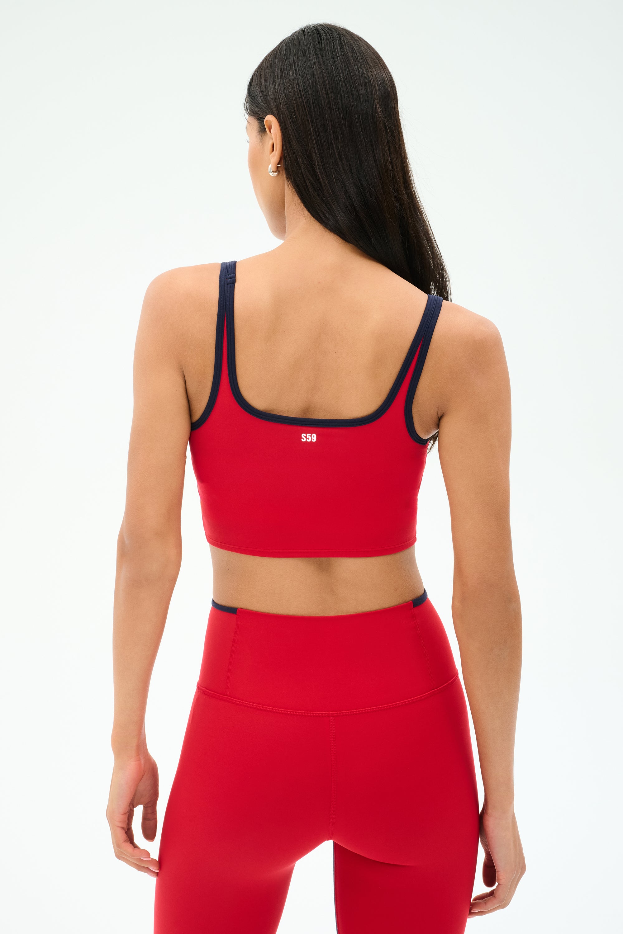 A person with long dark hair is seen from behind wearing the SPLITS59 Cait Rigor Bralette in Pirate Red/Indigo, paired with matching leggings, against a plain light background.