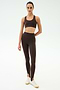 A person faces forward wearing the SPLITS59 Sara Airweight Bra in Dark Chocolate with matching high-waisted stirrup leggings and white sneakers, ready for Pilates or hot yoga, against a plain light background.