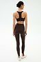 A woman stands facing away, wearing the SPLITS59 Sara Airweight Bra in Dark Chocolate with matching high-waisted leggings and white sneakers, perfect for Pilates, against a plain white background.