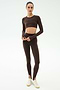A person wears the SPLITS59 Amelia Airweight Lite Shrug in Dark Chocolate, styled with matching high-waisted stirrup leggings and white sneakers, ideal for yoga or dance, against a plain background.