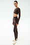 A person stands against a light background wearing the SPLITS59 Amelia Airweight Lite Shrug in Dark Chocolate paired with matching leggings and white sneakers—an ideal outfit for yoga or dance.