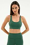 A woman models the SPLITS59 Ella Airweight Bra in Arugula/White, made from stretch fabric, standing with arms behind her back against a plain white background.