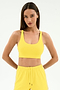 A woman wears the SPLITS59 Ella Airweight Bra in Bright Yellow/White with matching shorts, standing hands behind her back against a plain white background—ideal for hot yoga sessions.