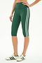 A person wears the SPLITS59 Ella High Waist Airweight Capri in Arugula/White with white sneakers featuring green stripes, standing against a plain background.