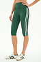 A person wears the SPLITS59 Ella High Waist Airweight Capri in Arugula/White with white sneakers featuring green stripes, standing against a plain background.