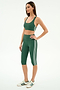 A woman stands in profile wearing the SPLITS59 Ella Airweight Bra in Arugula/White, paired with matching green capri leggings and white sneakers with green stripes. Both pieces are made from stretch nylon spandex athletic fabric.