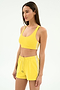 A woman in the SPLITS59 Ella Airweight Bra in Bright Yellow/White stands against a plain white background, paired with matching yellow athletic shorts featuring white stripes.