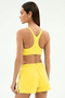 A woman stands with her back to the camera, wearing the SPLITS59 Ella Airweight Bra in Bright Yellow/White and matching shorts—an ideal outfit for hot yoga sessions.