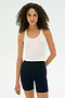 A person with curly hair wears the SPLITS59 Ashby Rib Crop tank in white and navy blue high-waisted shorts with red side stripes, standing against a plain light background.