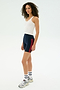 A woman models the SPLITS59 Ashby Rib Crop against a plain background, pairing it with navy cycling shorts featuring red stripes, white socks, and gray sneakers.